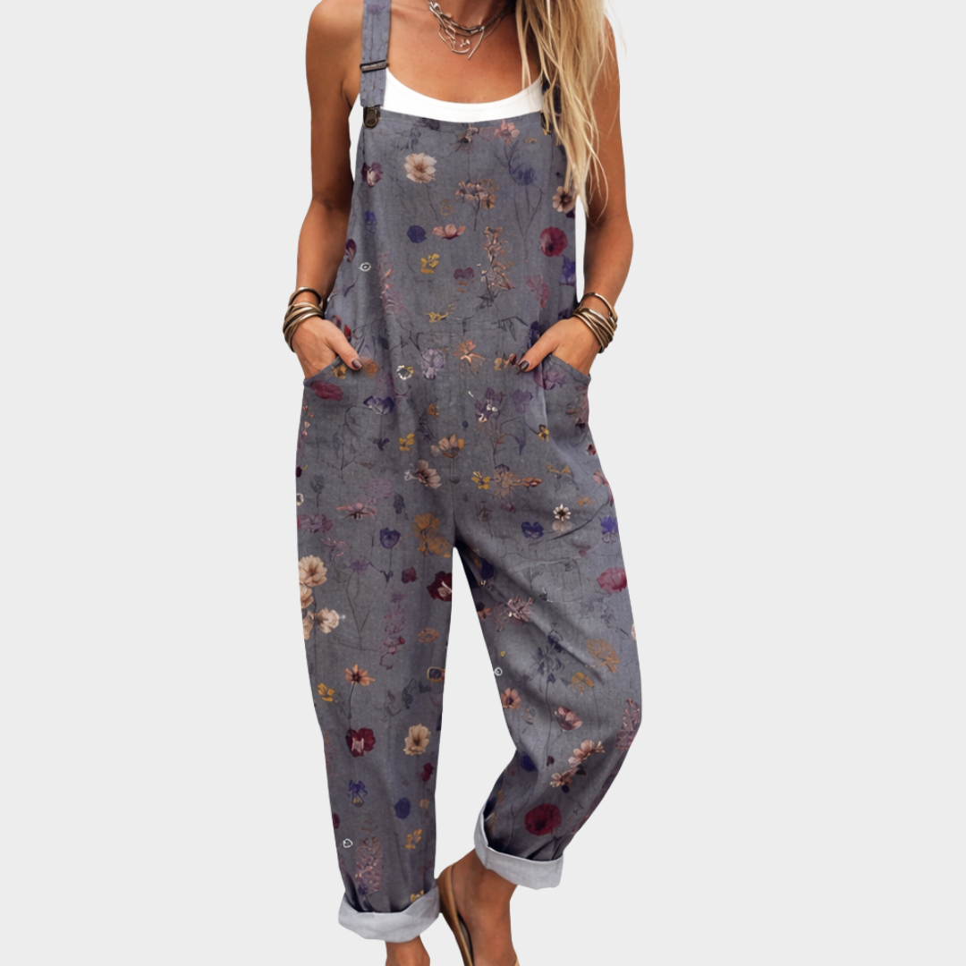 A woman wearing soft grey-blue overalls with a delicate scattered ditsy floral print and adjustable straps.