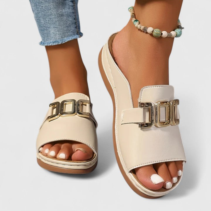A woman wearing white comfort slides with a golden front trim and a cushioned sole.