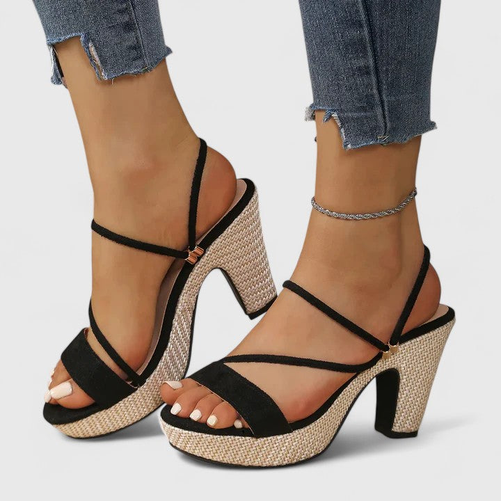 A woman in black strappy platform sandals with a chunky block heel, poised at an evening event.