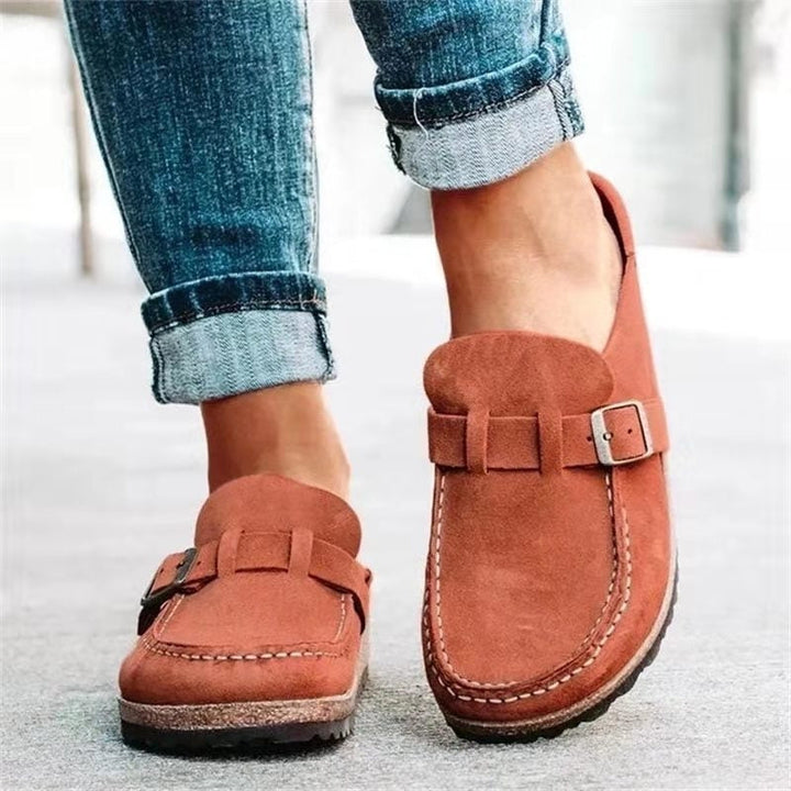 A woman wearing soft taupe buckle clog mules with cropped jeans on a city stroll.