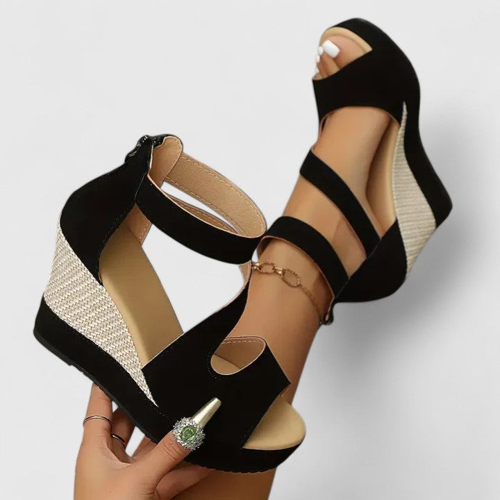 A woman in a summer dress wearing black crossover-strap heeled sandals, standing with easy confidence.
