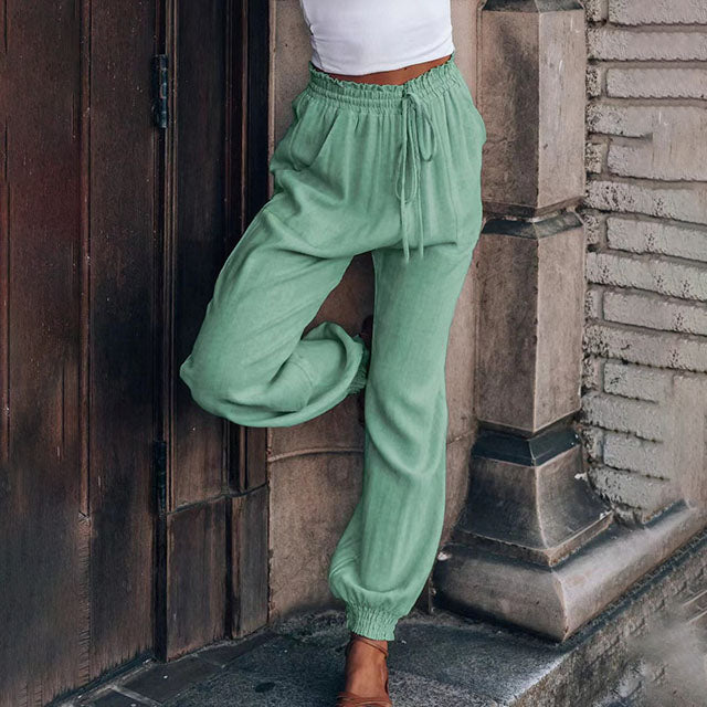 A woman wearing slim tapered black drawstring joggers with a high waist and front patch pockets.