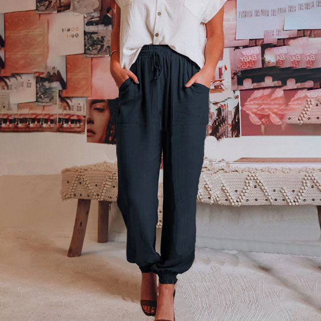 A woman wearing slim tapered black drawstring joggers with a high waist and front patch pockets.