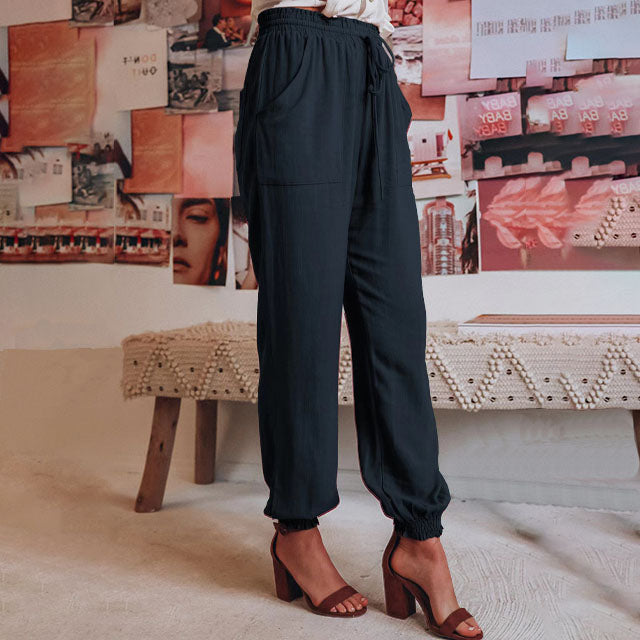 A woman wearing slim tapered black drawstring joggers with a high waist and front patch pockets.