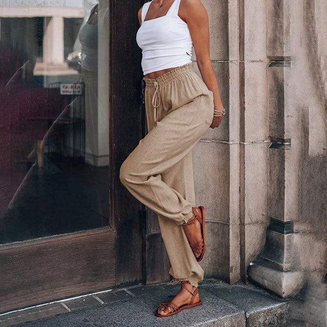 A woman wearing slim tapered black drawstring joggers with a high waist and front patch pockets.
