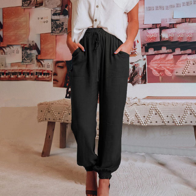 A woman wearing slim tapered black drawstring joggers with a high waist and front patch pockets.