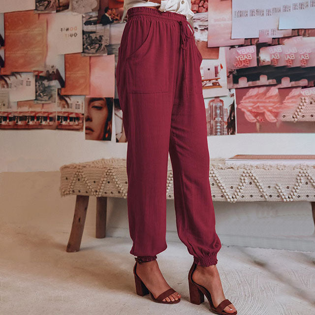 A woman wearing slim tapered black drawstring joggers with a high waist and front patch pockets.