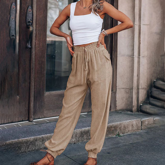 A woman wearing slim tapered black drawstring joggers with a high waist and front patch pockets.