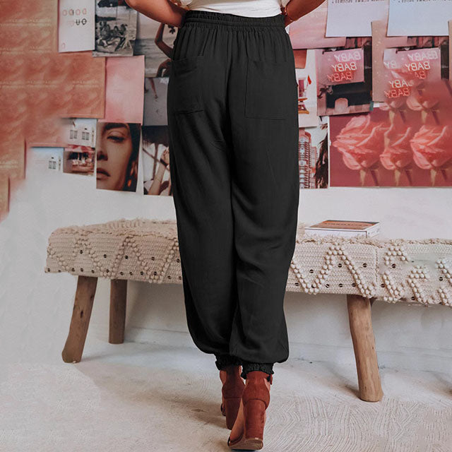 A woman wearing slim tapered black drawstring joggers with a high waist and front patch pockets.