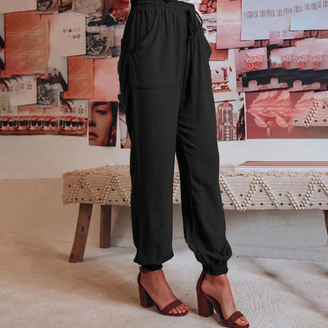 A woman wearing slim tapered black drawstring joggers with a high waist and front patch pockets.