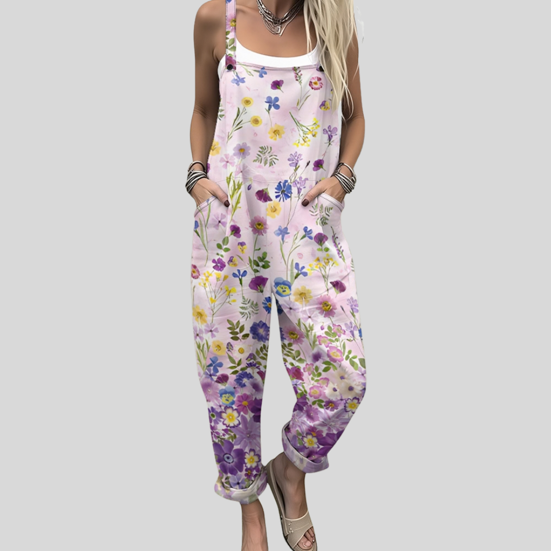 A woman wearing white overalls printed with delicate violet, yellow and pink wildflowers, relaxed outdoors.