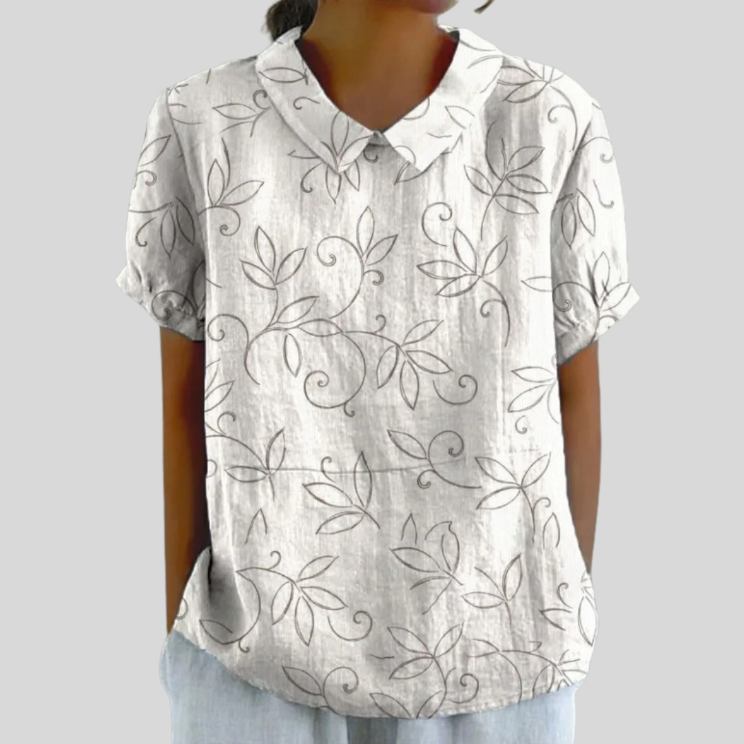 A woman wearing a relaxed cream top with a delicate leaf-and-vine print and a polo collar, moving comfortably through her day.