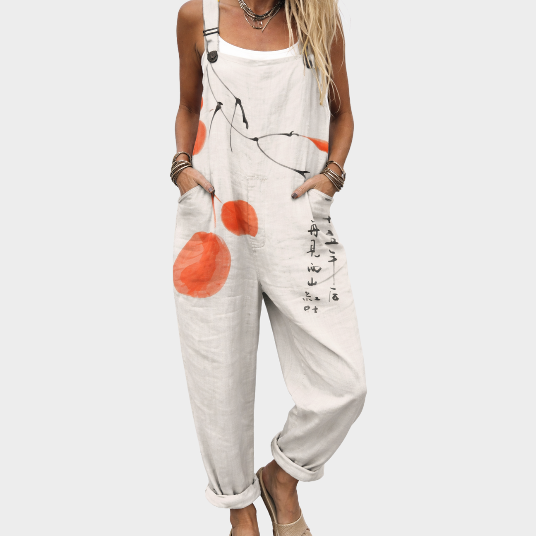 Woman wearing cream overalls with a painted orange fruit and ink branch print, adjustable straps, calm and relaxed.