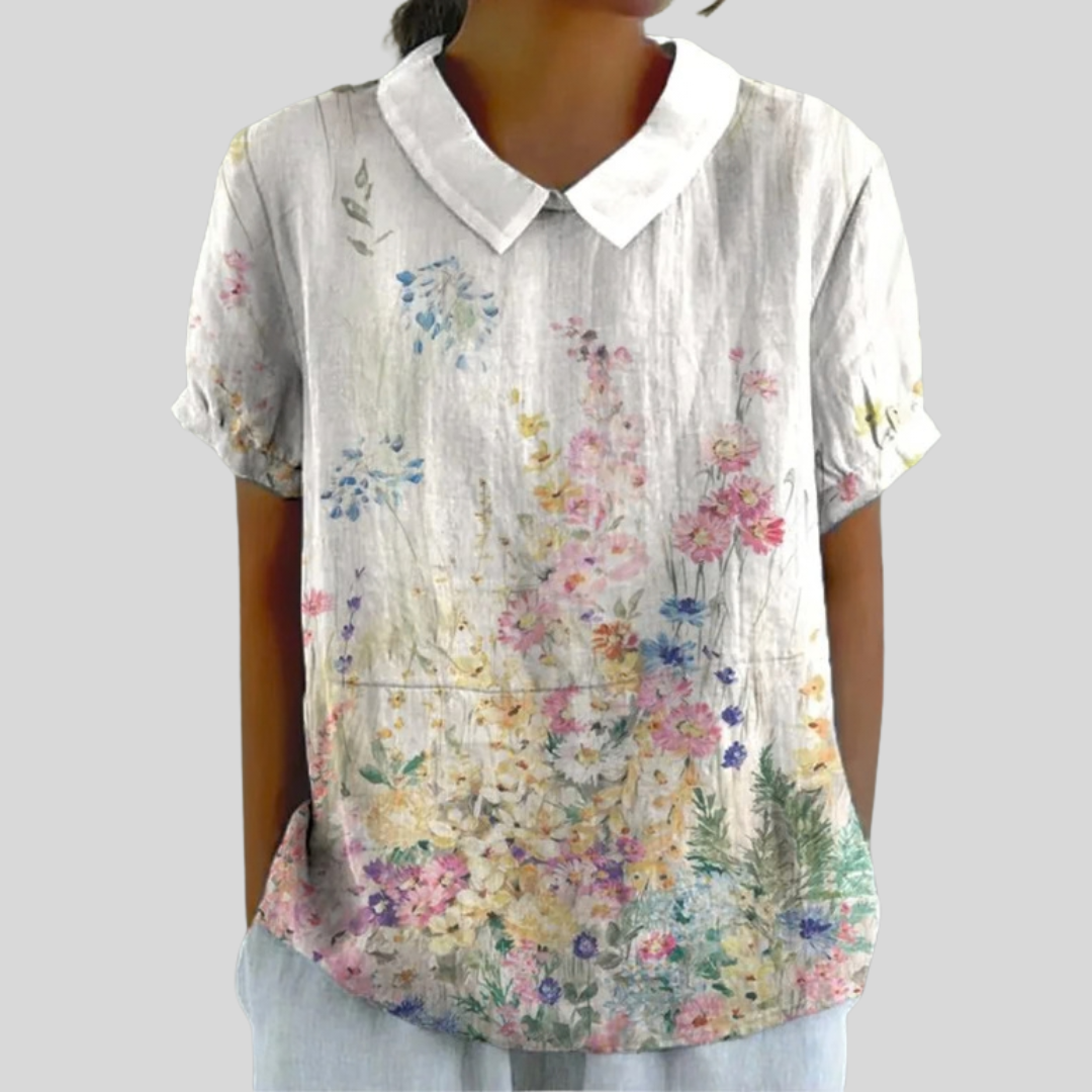 A woman wearing a flowing floral top with a polo collar, looking elegant and at ease.