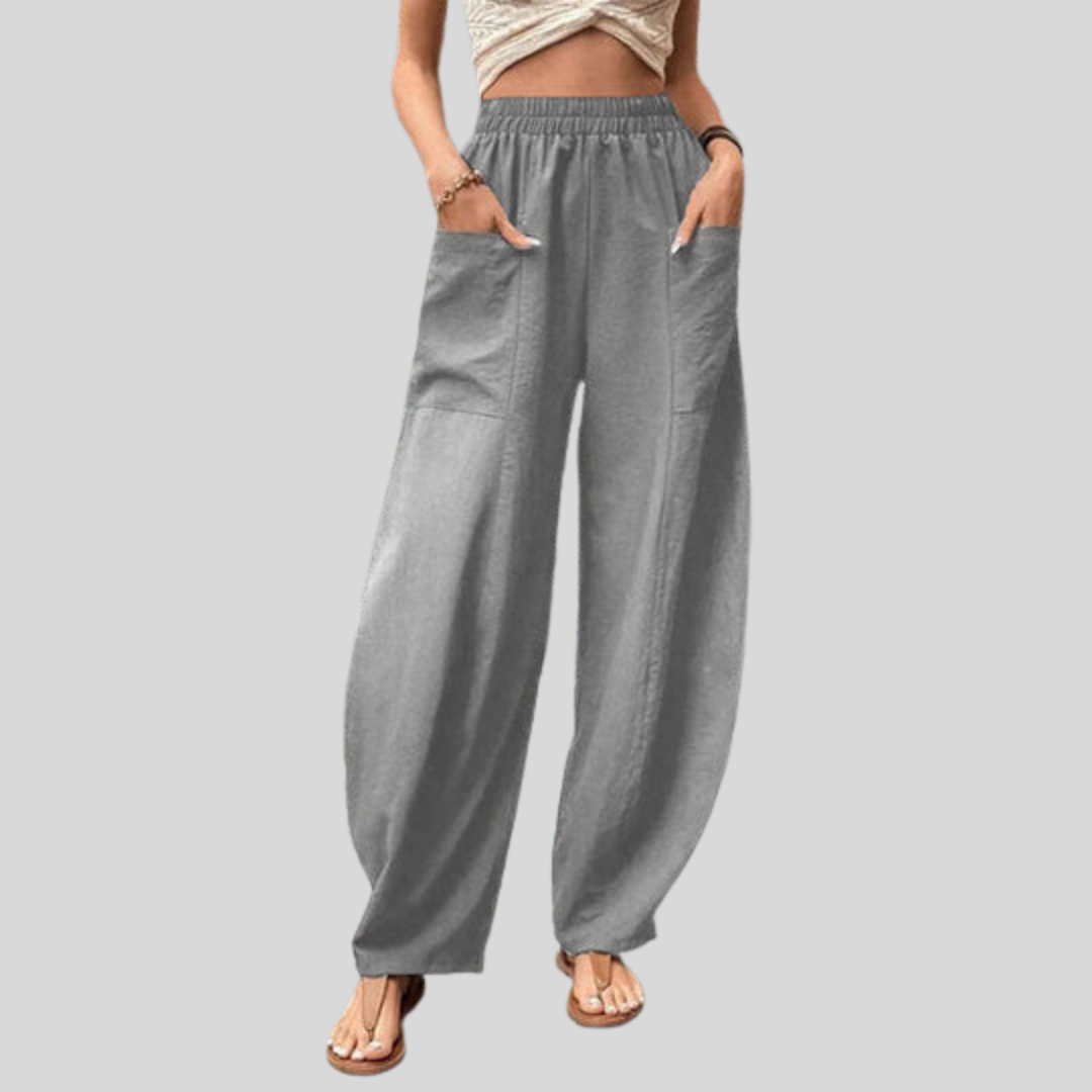 A woman walking in flowing wide-leg pants with big patch pockets and an elegant, draped silhouette.