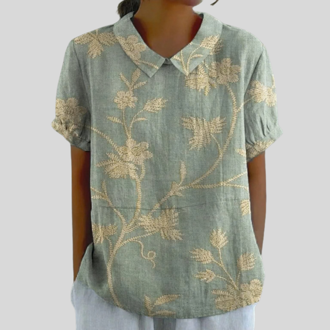 A woman wearing a flowing floral top with a neat polo collar, styled for an easy everyday look.