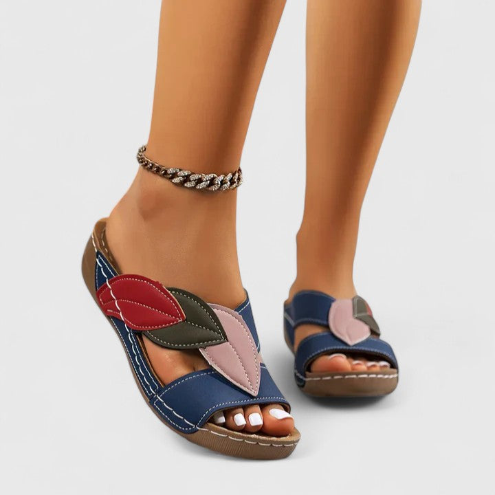 A woman wearing colourful leaf-print sandals with a cushioned insole and easy slip-on design.