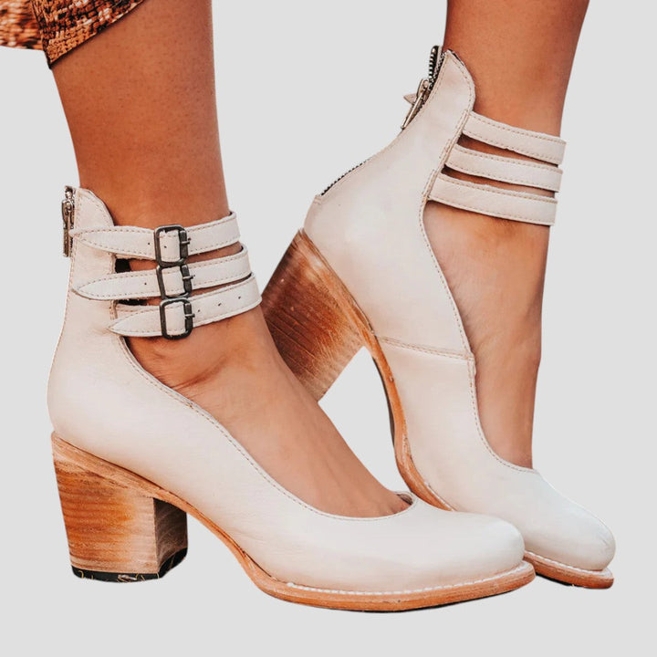A woman wearing cognac block-heel pumps with triple ankle straps and a rounded toe.