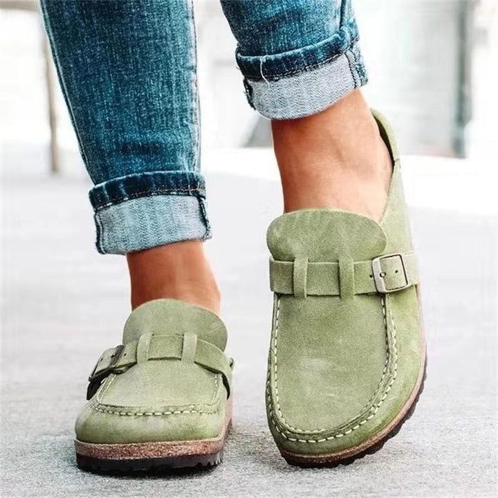 A woman wearing soft taupe buckle clog mules with cropped jeans on a city stroll.