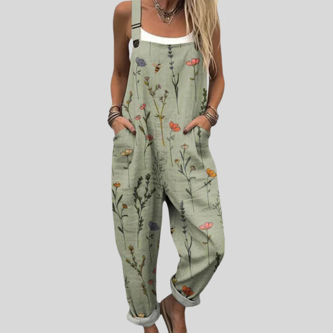 A woman in sage green overalls with a delicate wildflower print, a white top and sandals.