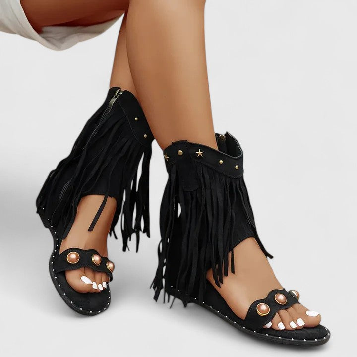 A woman wearing khaki fringe wedge sandals with a fringed ankle cuff and a back zip.