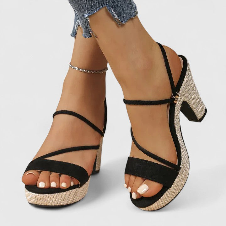 A woman in black strappy platform sandals with a chunky block heel, poised at an evening event.