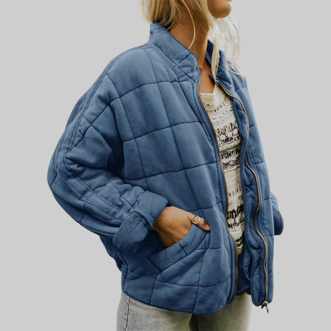 A woman wearing an oversized blush pink quilted jacket with a stand collar and zip front, hand in the pocket.