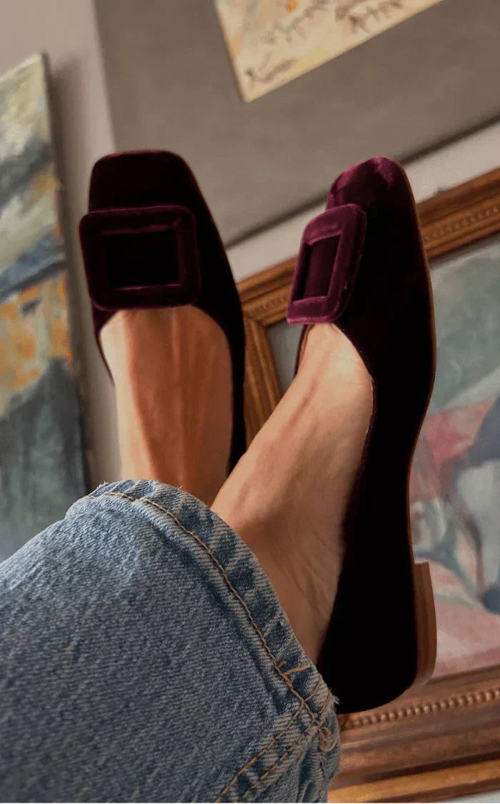 A woman wearing soft, velvety-finish loafers in a rich tone with tailored pants, looking refined and relaxed.