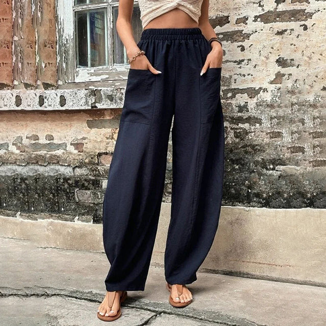 A woman walking in flowing wide-leg pants with big patch pockets and an elegant, draped silhouette.