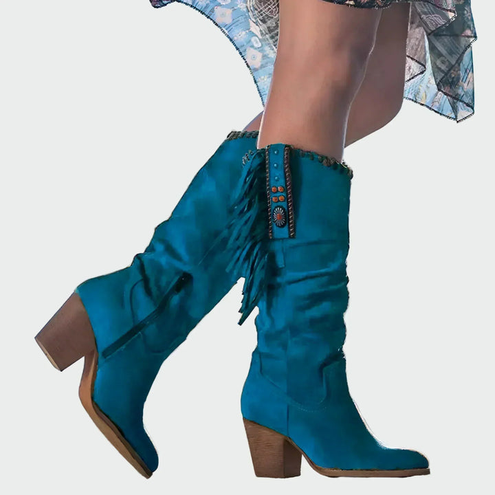 Woman wearing tan fringed boho-Western knee-high boots with a floaty dress at a festival.