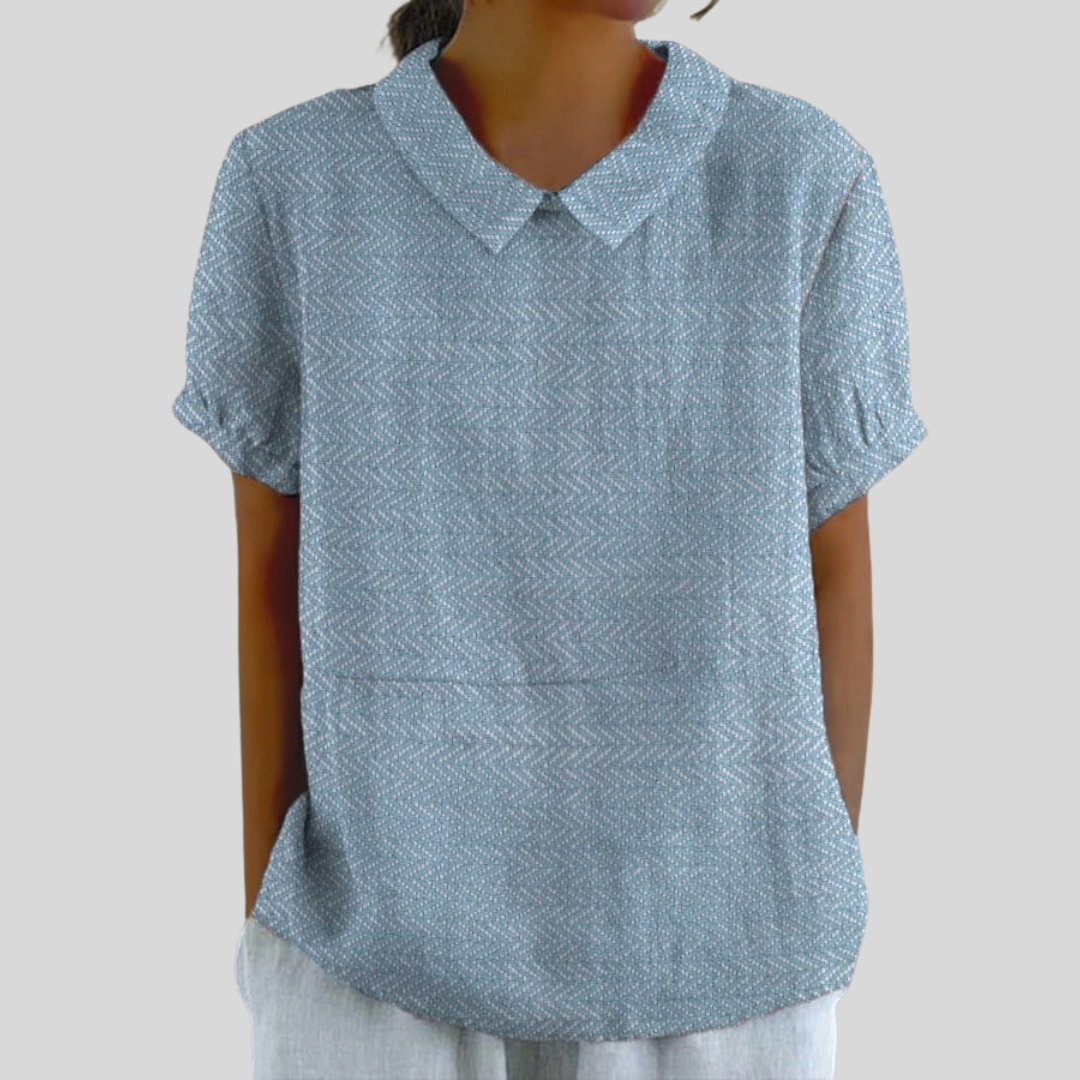 A woman wearing a soft blue collared top with a fine texture and refined collar, paired with smart pants.