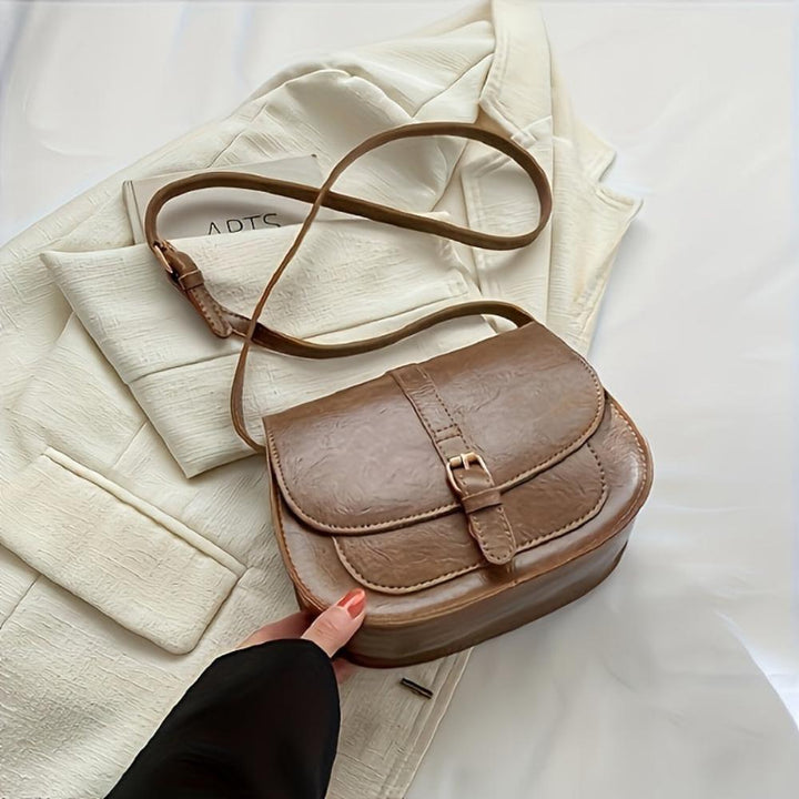 A woman carrying a crossbody satchel at her hip while out for a walk in town.