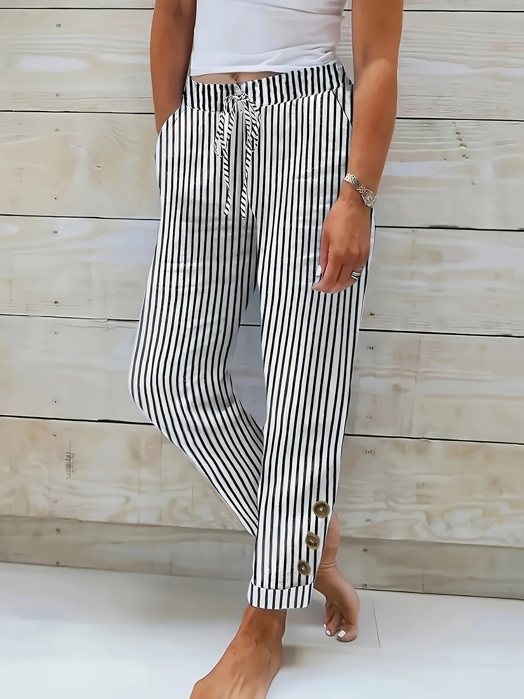 A woman wearing black vertical-striped pants with a drawstring waist and button hem detail.