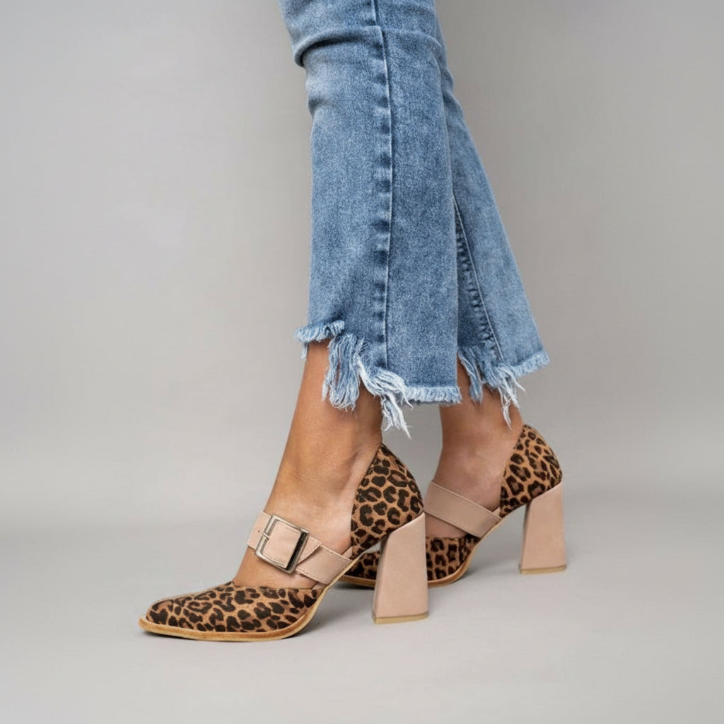 A woman wearing leopard print pointed-toe heels with a wide nude buckle strap and a neutral block heel.