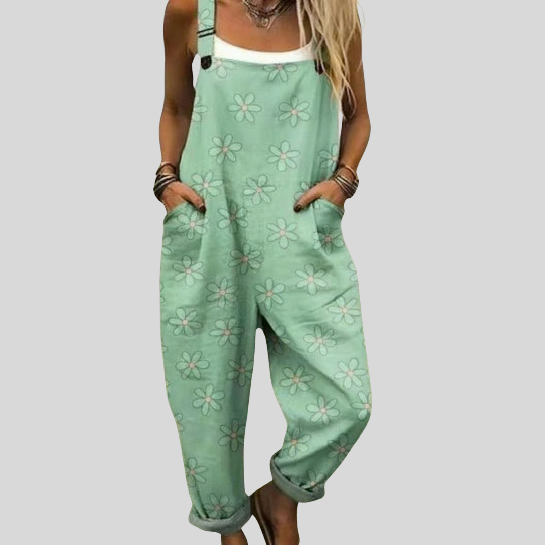 A woman wearing soft mint green overalls printed with delicate white flowers, relaxed by the water.