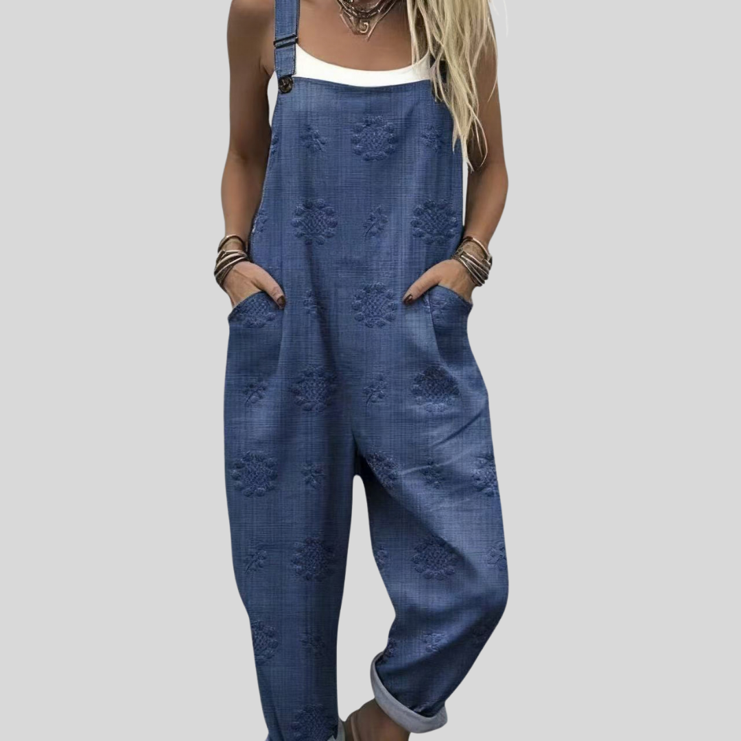 A woman wearing relaxed washed-blue overalls with raised tone-on-tone flower motifs and a white top.