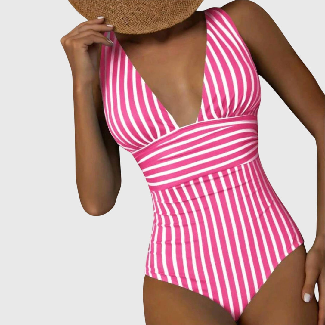 A woman by the sea in a beige and white striped V-neck swimsuit, relaxed and glowing in the sun.