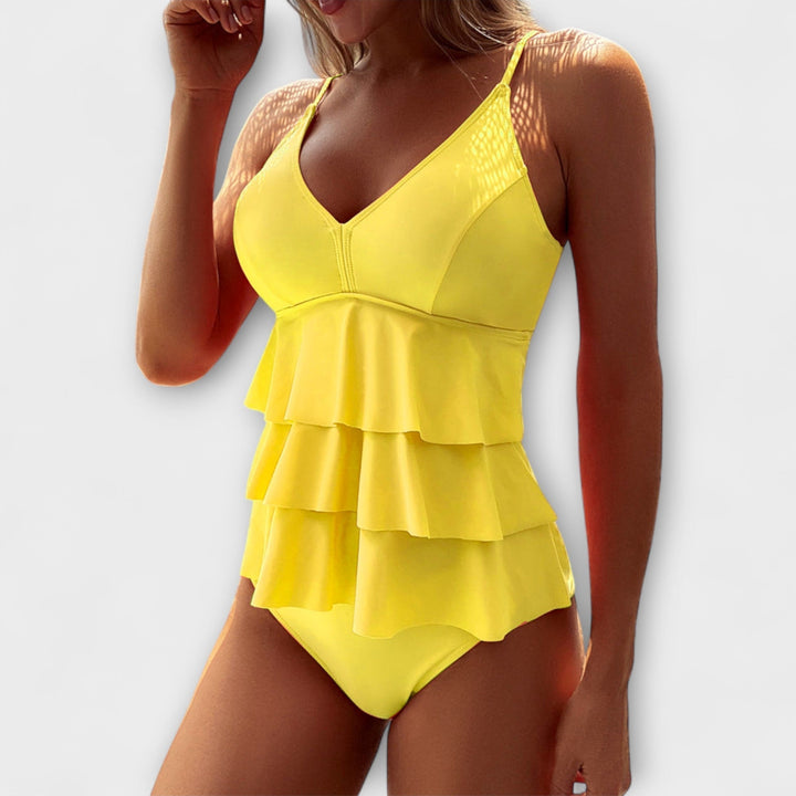 A woman by the pool in a solid-colour tiered ruffle swimsuit, poised and relaxed in the summer sun.