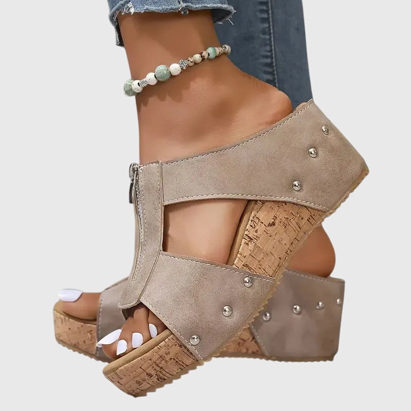 A woman wearing black zip-front wedge mules with a cushioned footbed and a broad platform sole.