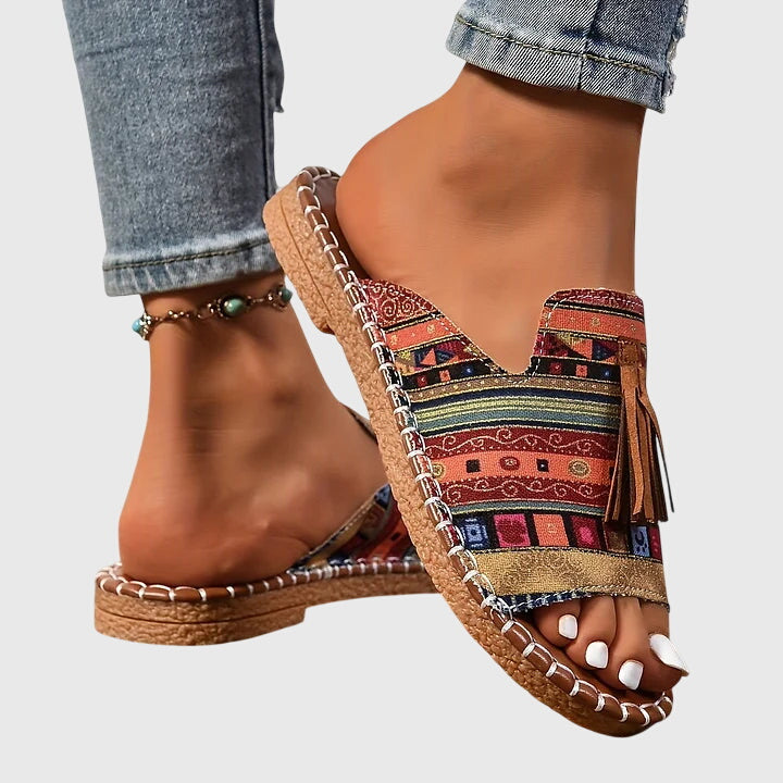 A woman wearing colourful patterned boho slides with tassel details on a holiday day out.