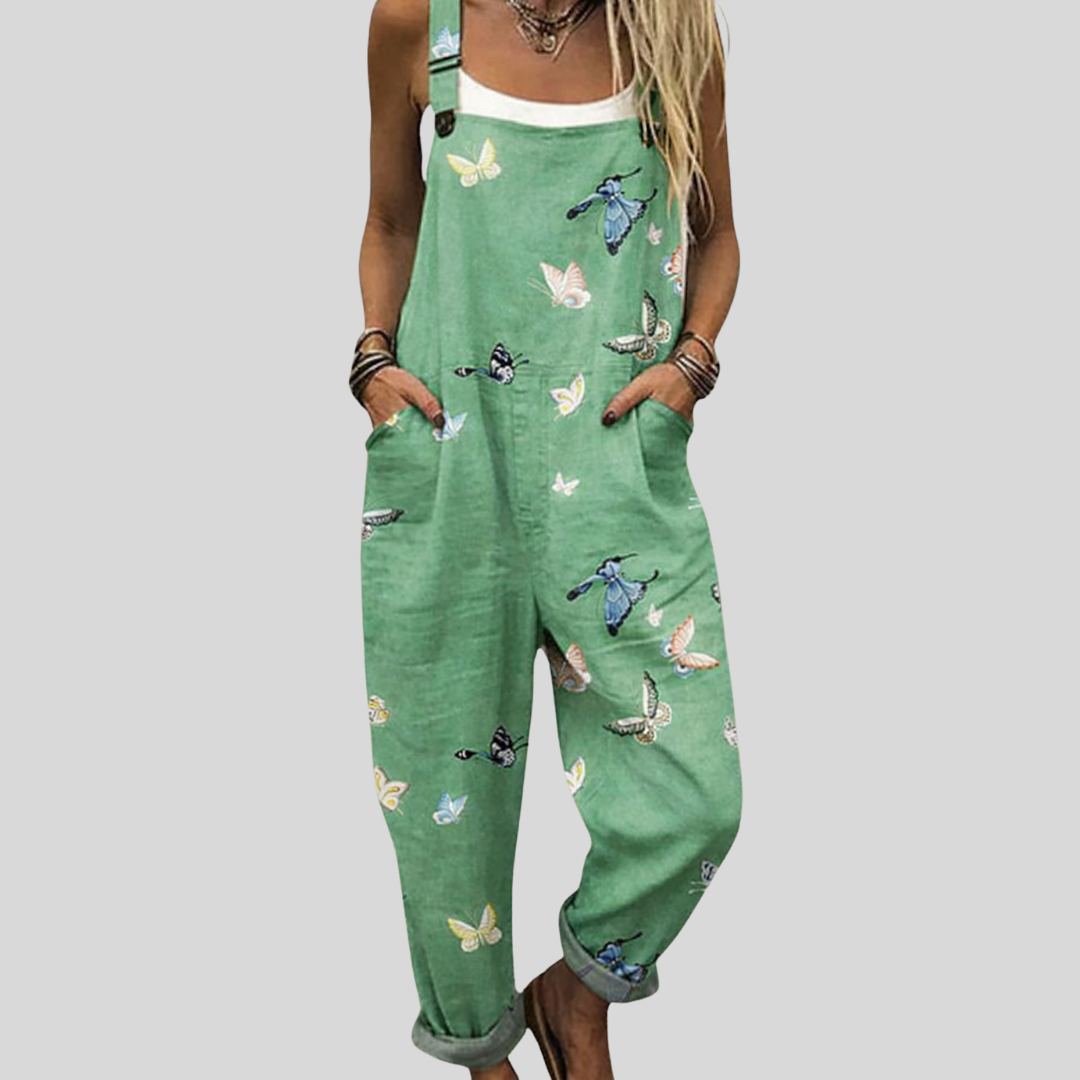 A woman wearing green overalls with a delicate butterfly print, relaxed and smiling on a bright day.