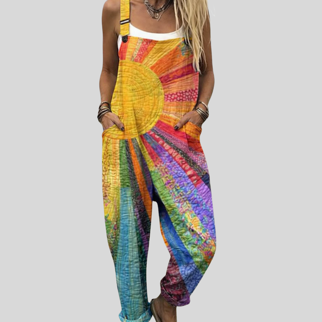 Woman wearing colourful tie-dye overalls with a sun and rainbow design, smiling on a bright summer day.