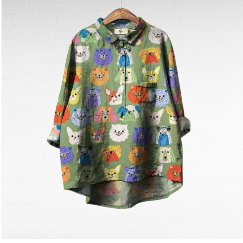 A relaxed blue button-up blouse printed with playful brown cartoon dachshunds and a small flower, shown on a hanger.