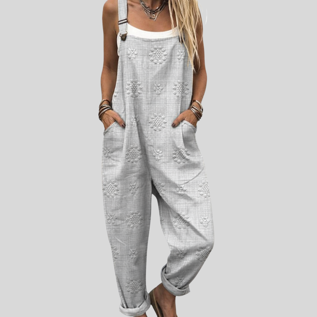 A woman wearing soft grey overalls with a subtle tone-on-tone floral pattern and a blouse.