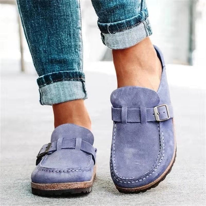 A woman wearing soft taupe buckle clog mules with cropped jeans on a city stroll.