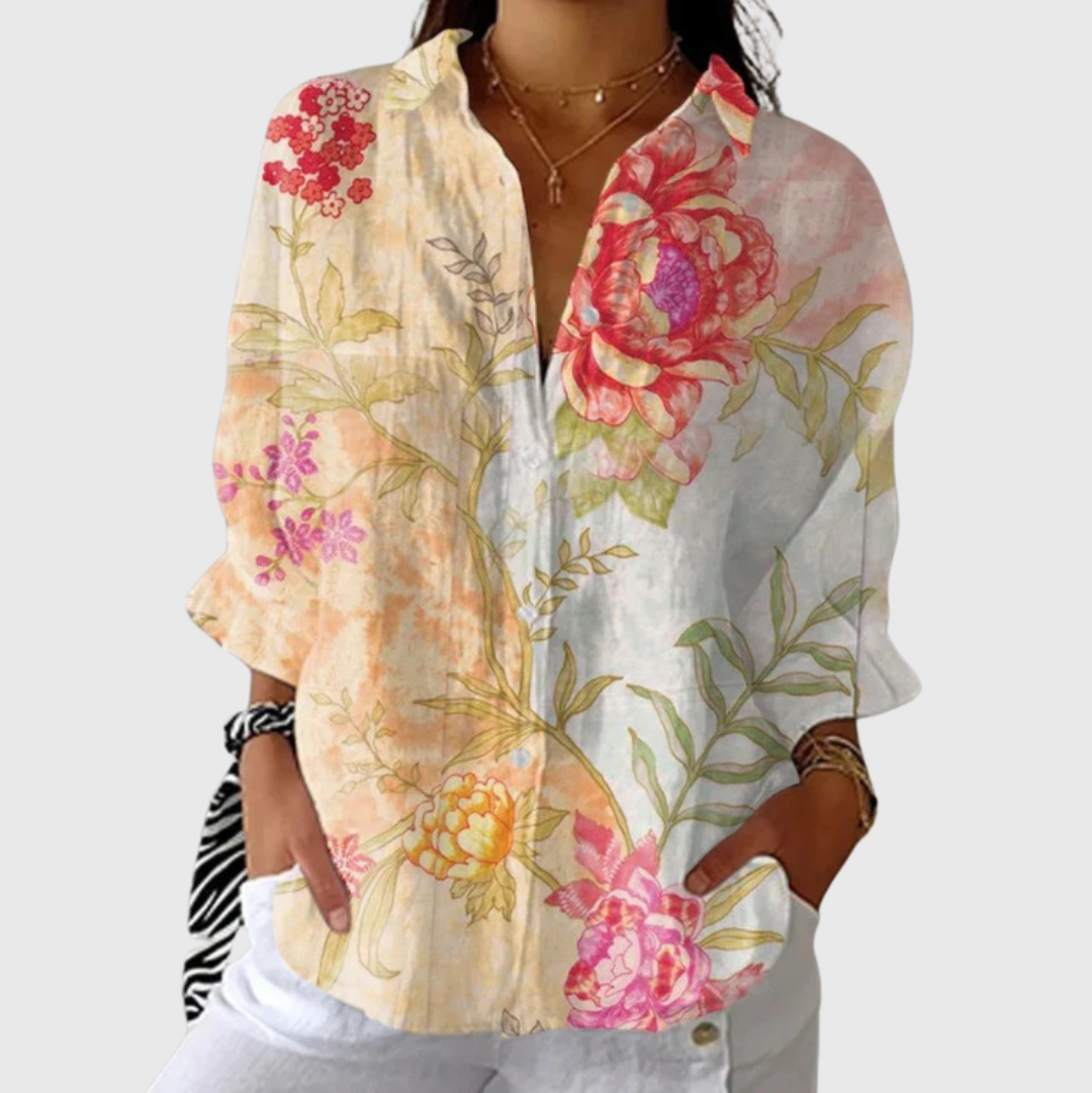 A woman in a colourful floral blouse worn loose with pants, smiling