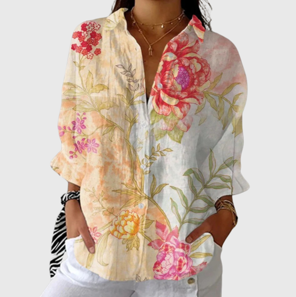 A woman in a colourful floral blouse worn loose with pants, smiling