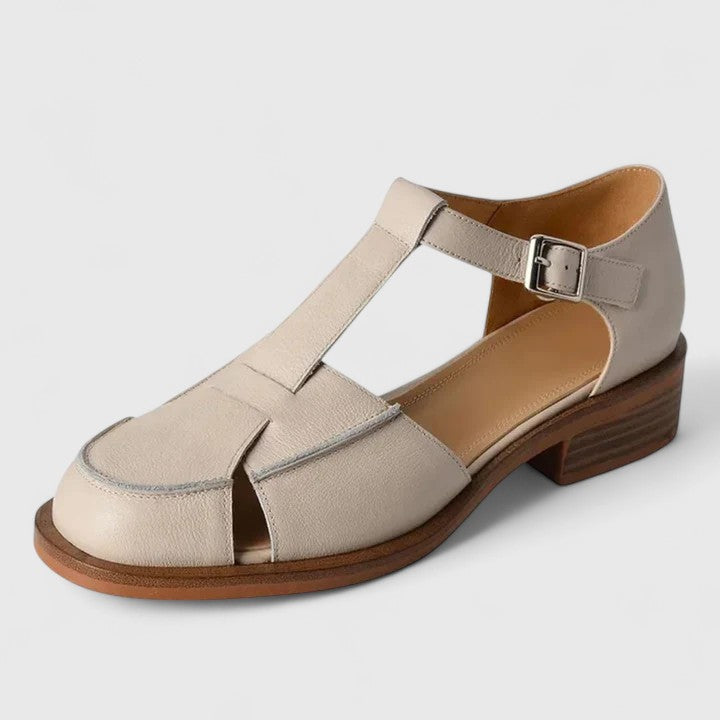 Woman wearing beige strapped Mary Jane sandals on a sunny terrace.