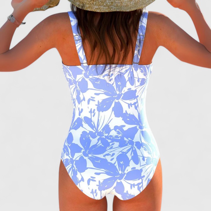 A woman by the water in an elegant printed swimsuit, poised and confident in the summer sun.