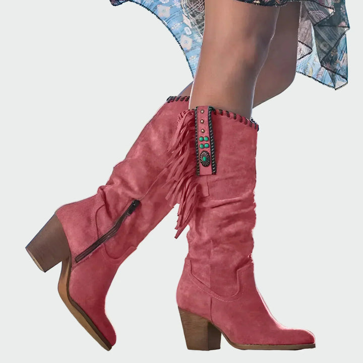 Woman wearing tan fringed boho-Western knee-high boots with a floaty dress at a festival.